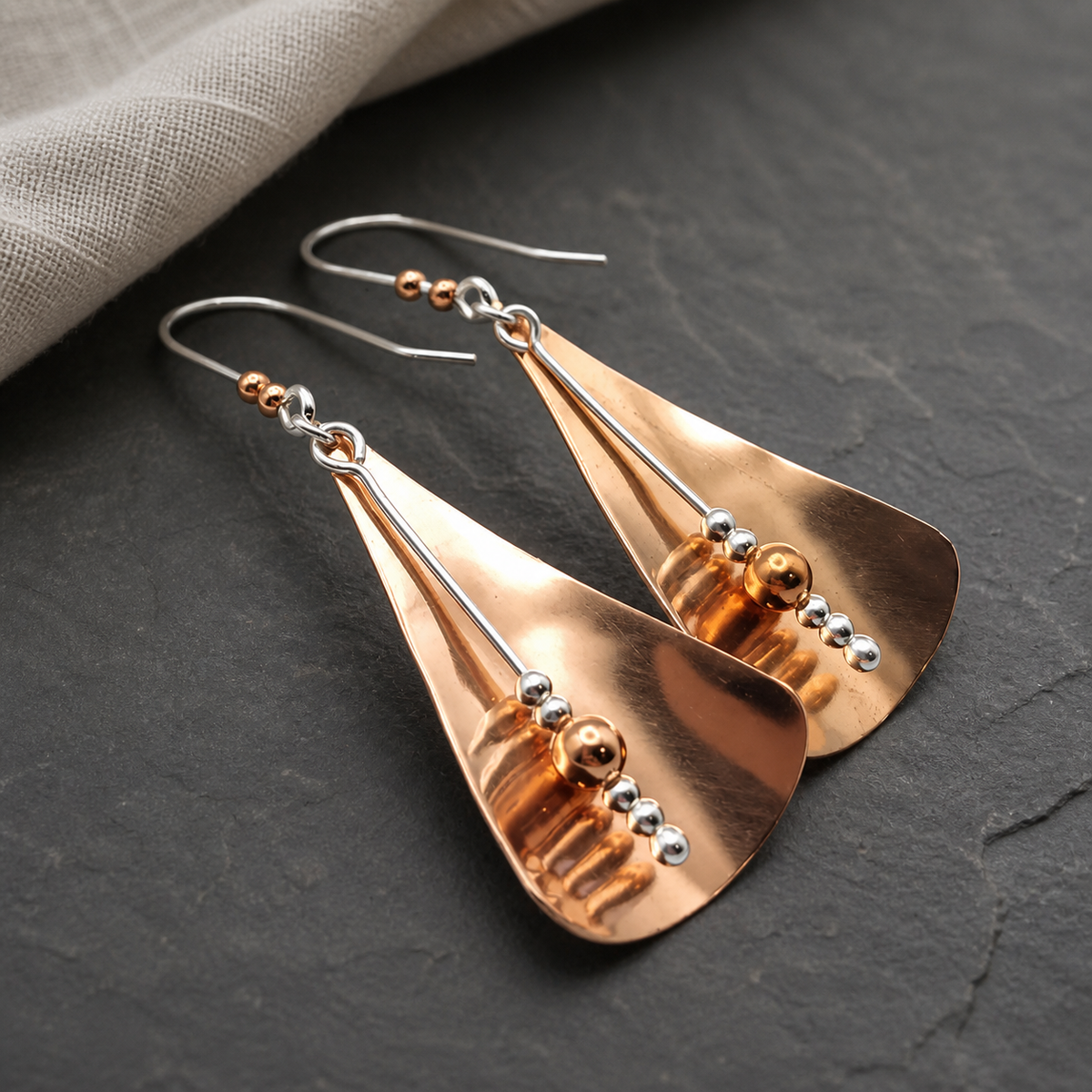 Copper and sterling silver triangle earrings displayed on dark natural stone