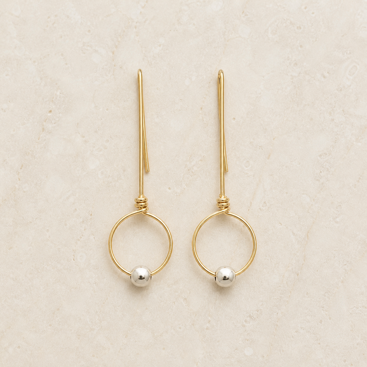Gold-filled threader hoop earrings with silver beads on a warm ivory background