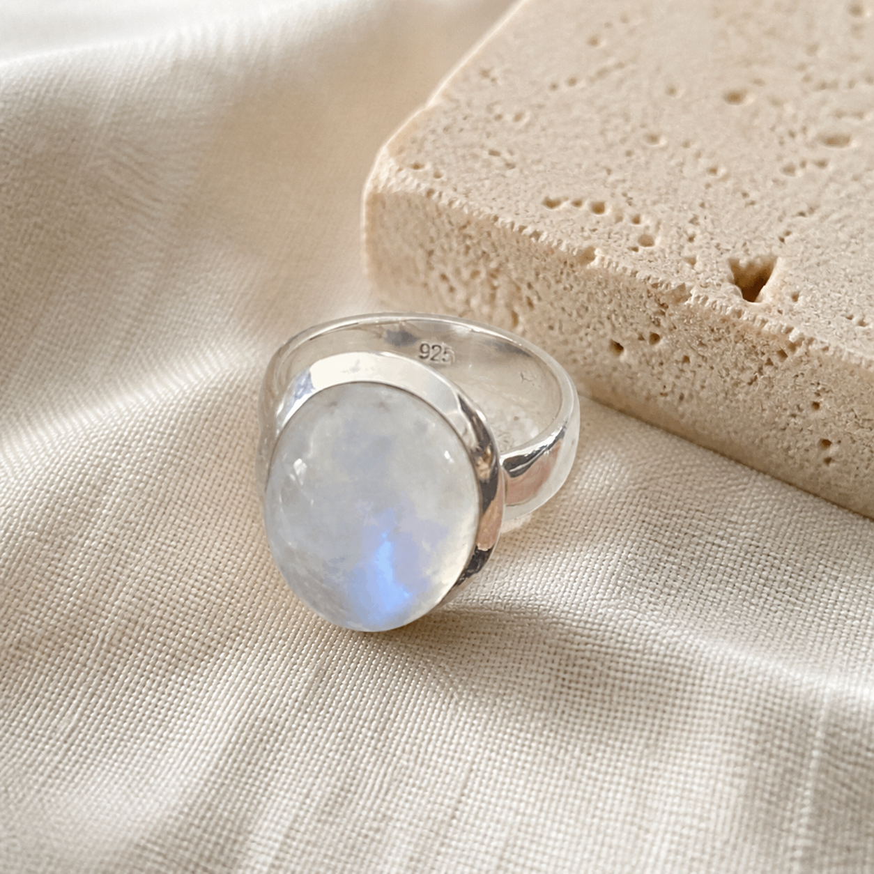 Sterling silver oval moonstone ring displayed on warm ivory linen