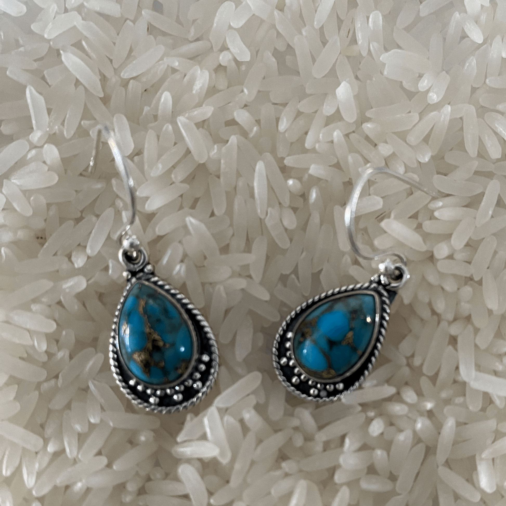 Bohemian-inspired sterling silver earrings featuring vibrant turquoise teardrops, encased in delicate silver settings with traditional beaded accents, offering a pop of color and boho chic to any look.