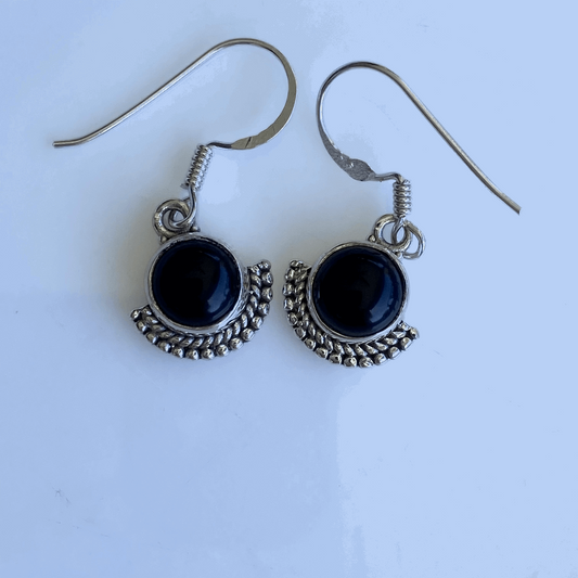 Distinctive earrings with a glossy black onyx stone set above a sterling silver crescent moon design, featuring beaded details to accentuate the crescent's curves, hanging from silver hooks.