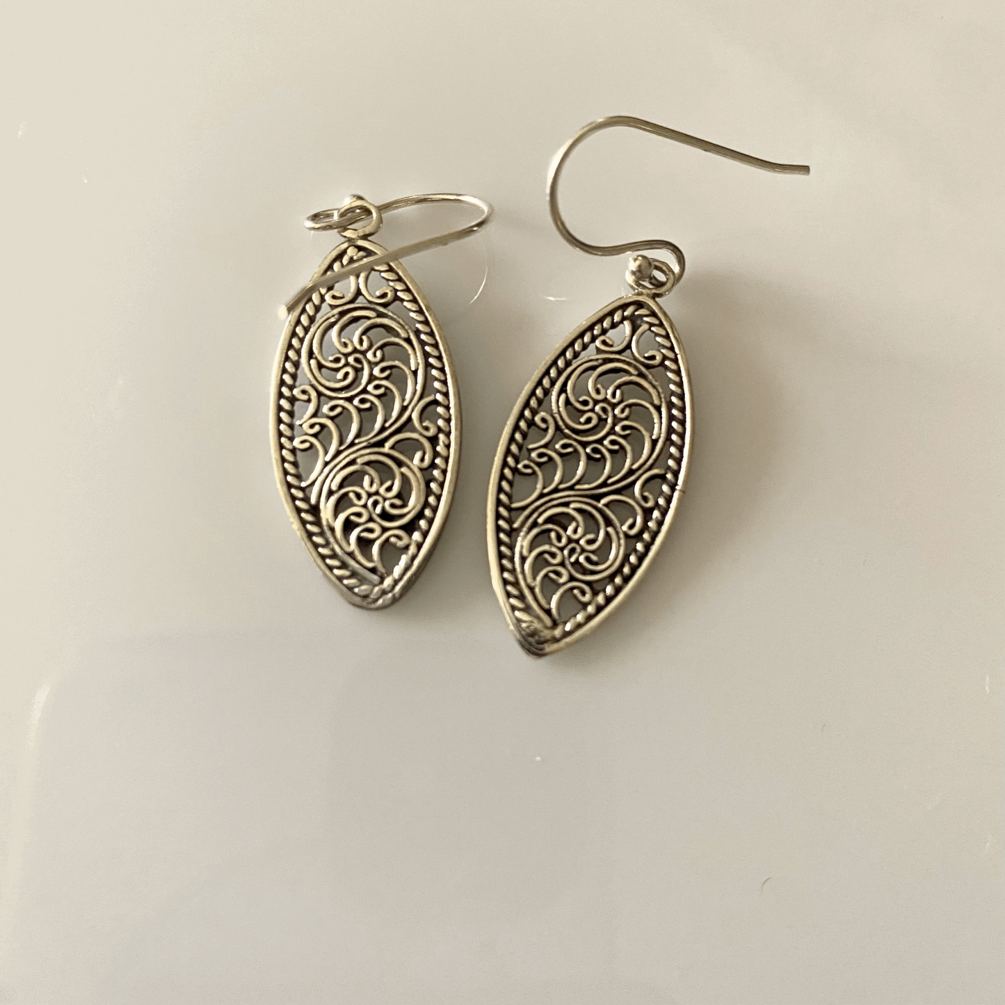 Intricately crafted sterling silver drop earrings featuring an elegant swirl filigree design that exudes a vintage charm, suspended from simple ear hooks for a graceful dangle.