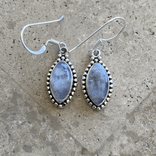 Elegant Chic Moonstone Teardrop Earrings with a soft blue sheen, set in sterling silver with intricate detailing, hanging from classic hook ear wires.