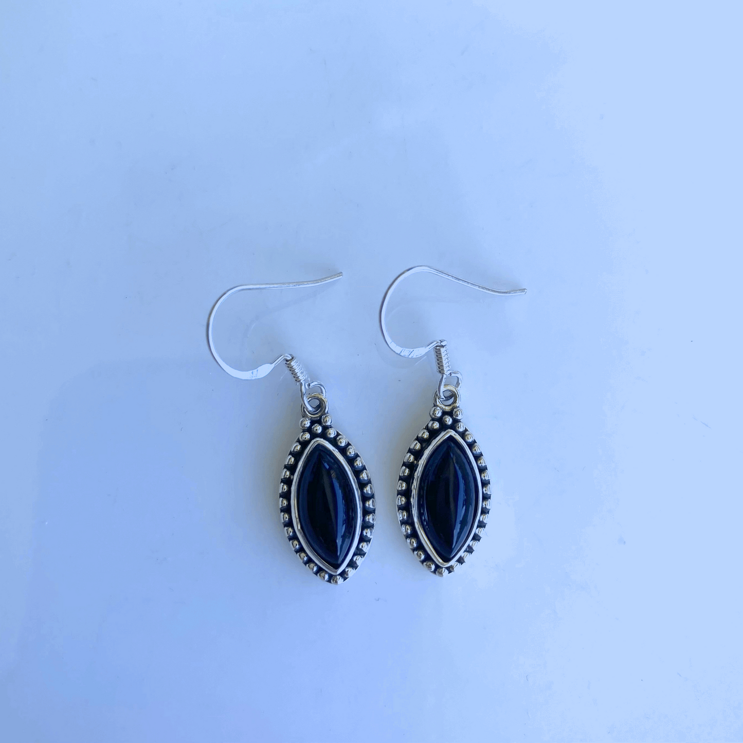 Sophisticated teardrop earrings with polished black onyx stones, set in a detailed sterling silver bezel with a delicate beaded border, suspended from silver ear wires for an elegant dangle.