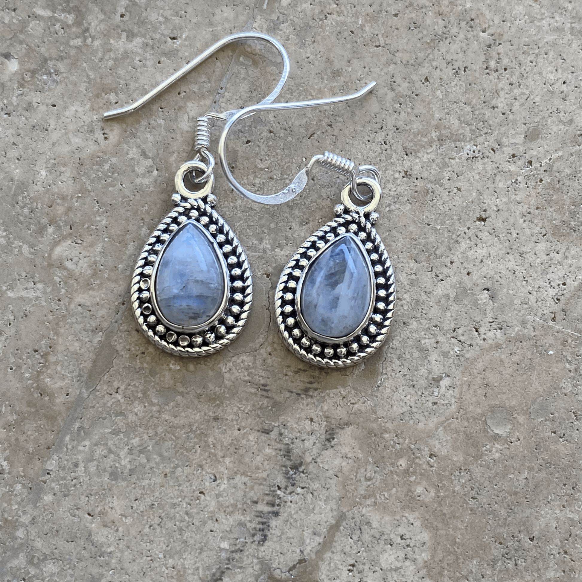 A pair of Radiant Moonstone Teardrop Earrings, featuring luminous, pearlescent moonstones encased in polished sterling silver settings with classic beaded details, dangling from elegant hooks.