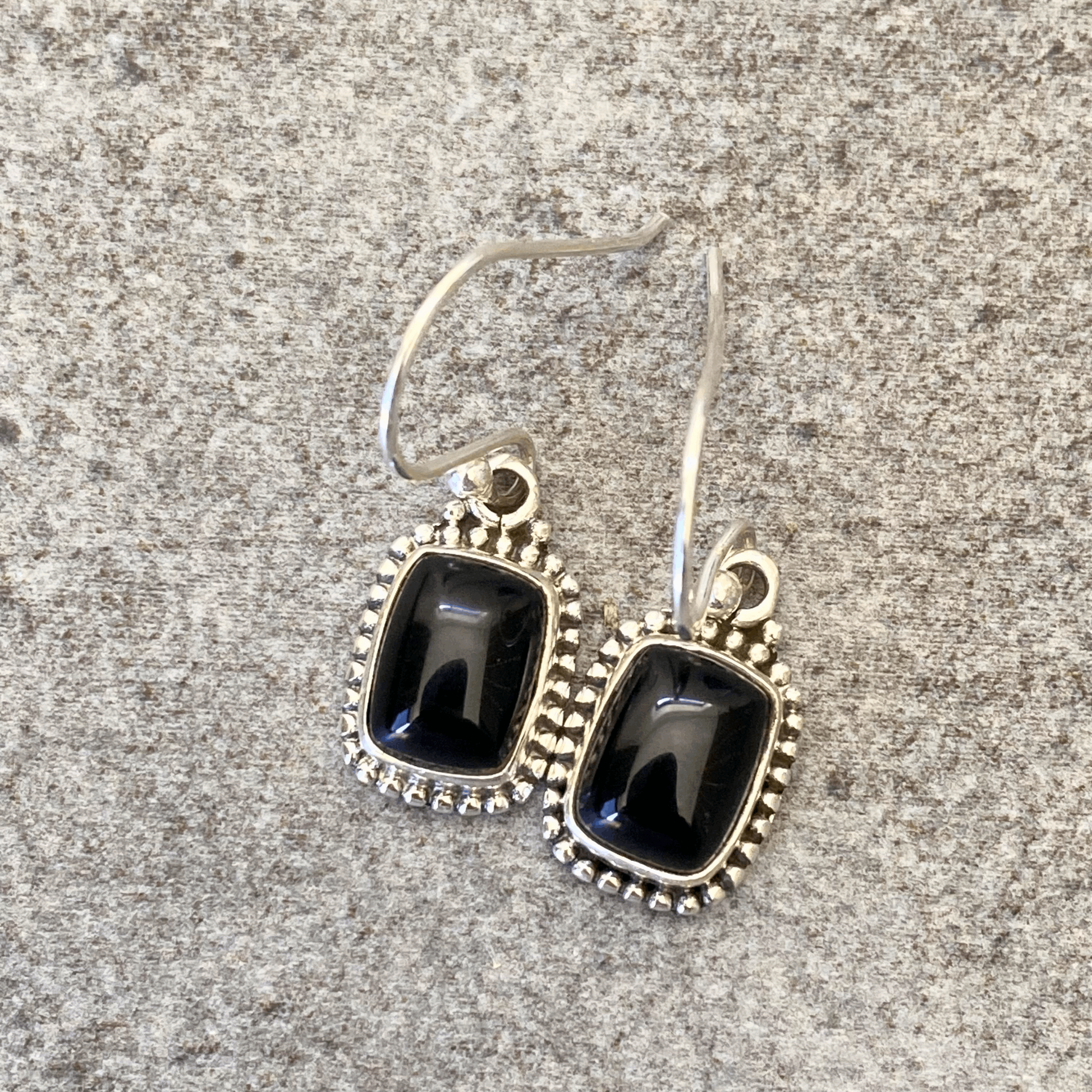 Elegant earrings showcasing sleek black onyx rectangles with a smooth finish, framed by sterling silver with a detailed beaded design, hanging gracefully from silver hooks.