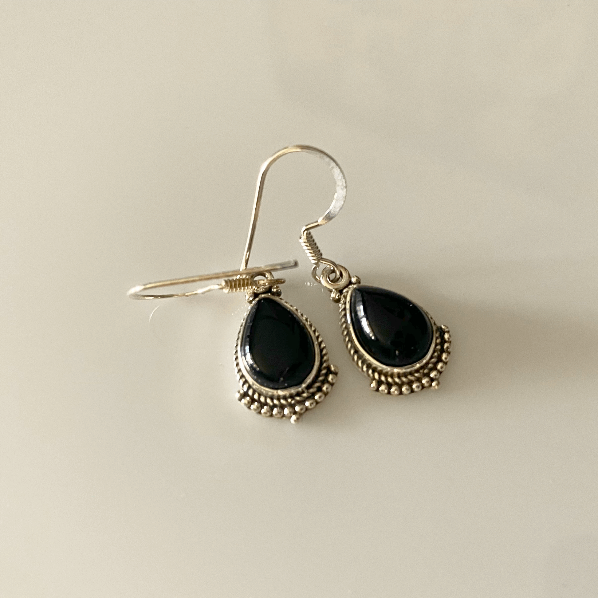 A pair of Classic Black Onyx Teardrop Dangle Earrings, featuring polished, deep black gemstones set in sterling silver with intricate beaded detailing along the edges, suspended from silver hooks.