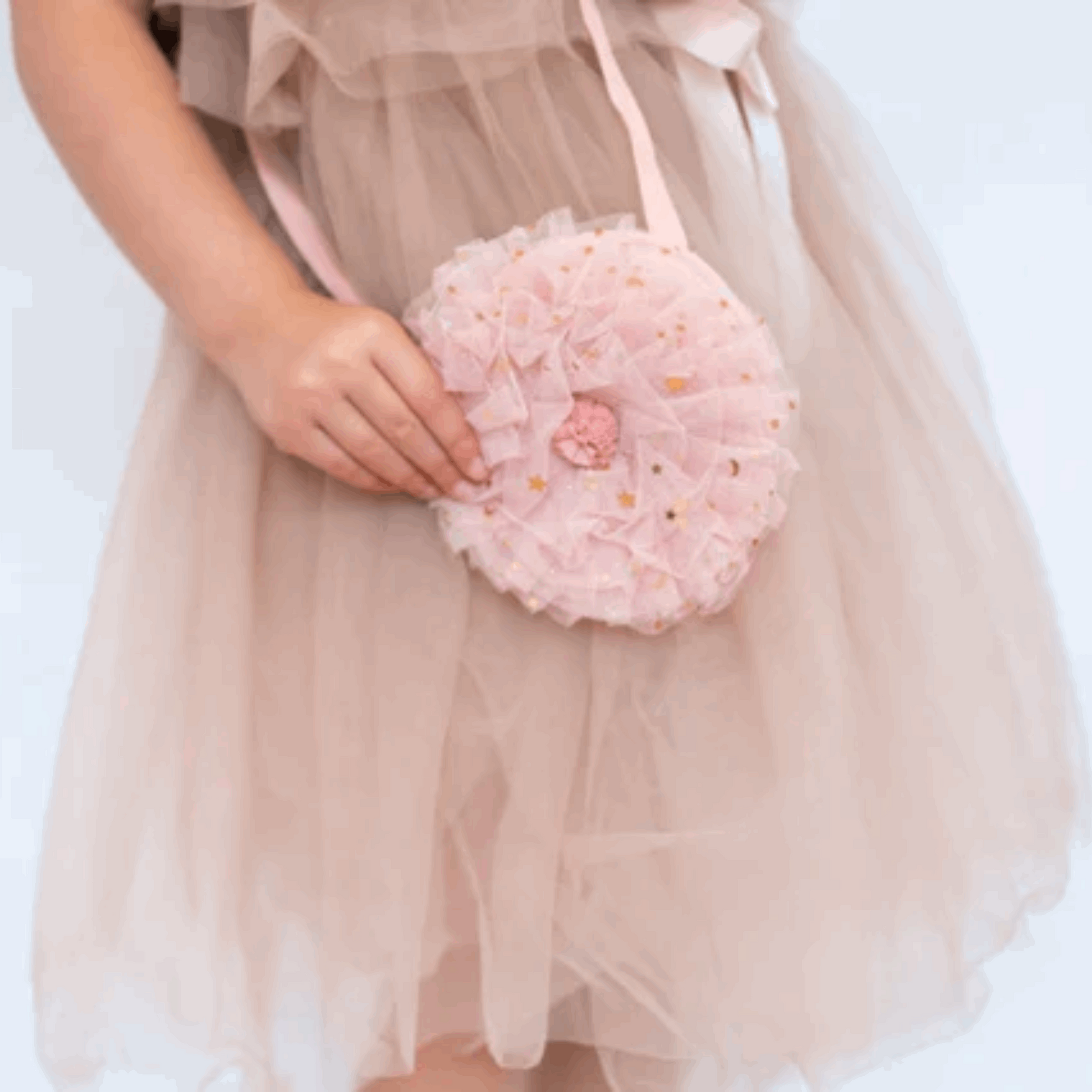 A child holding a Pixie Dust Tulle Ruffle Bag in pink, with layers of sparkling tulle and a decorative rosette, paired with a soft tulle dress.