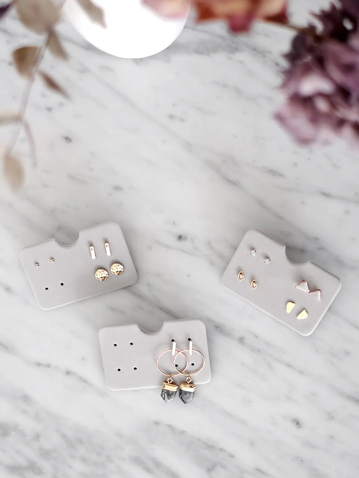 Three grey velvet Stackers earring holders arranged with earrings on a marble surface. Jewellery not included.