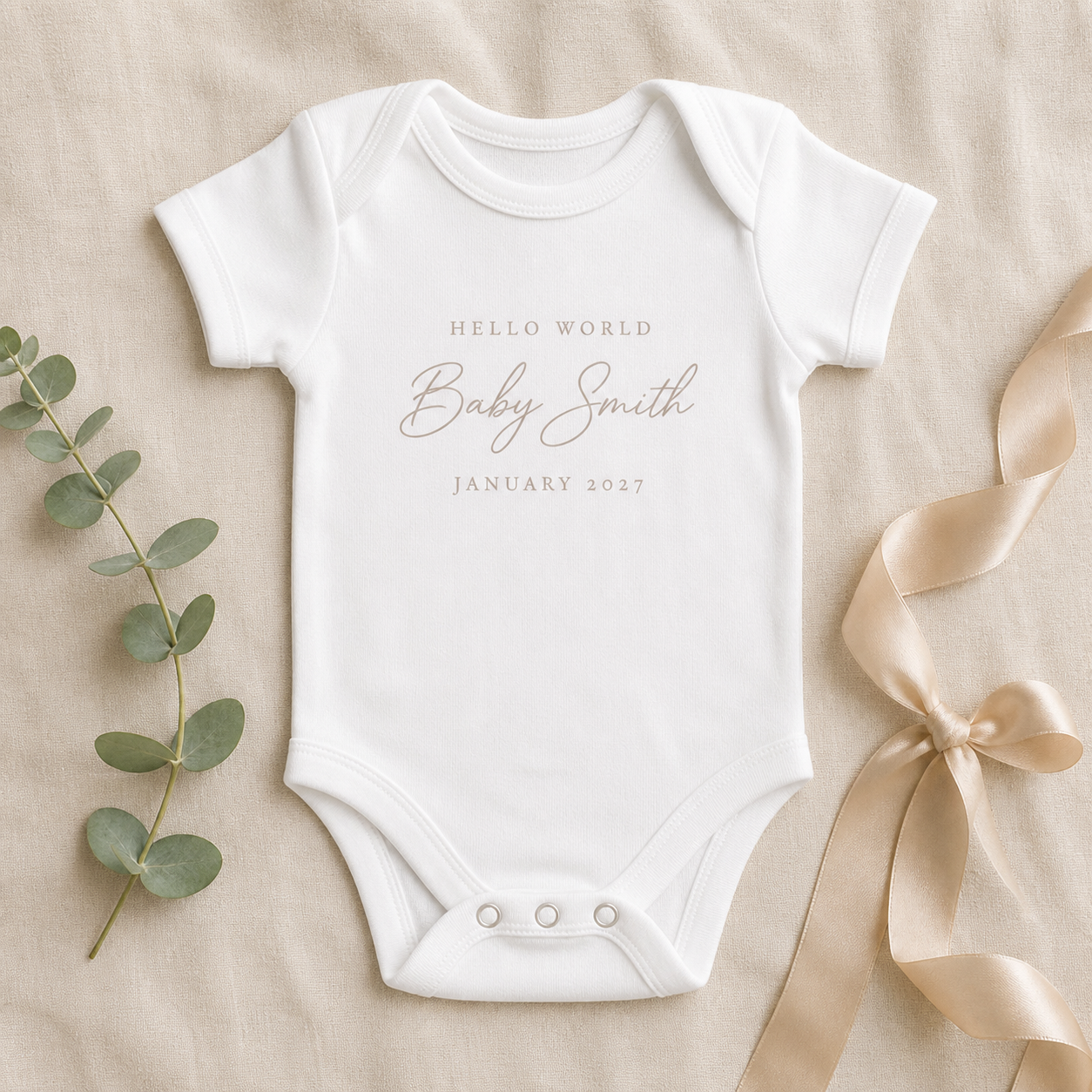 Concept mockup of a white personalised baby announcement bodysuit reading Hello World, Baby Smith, January 2027
