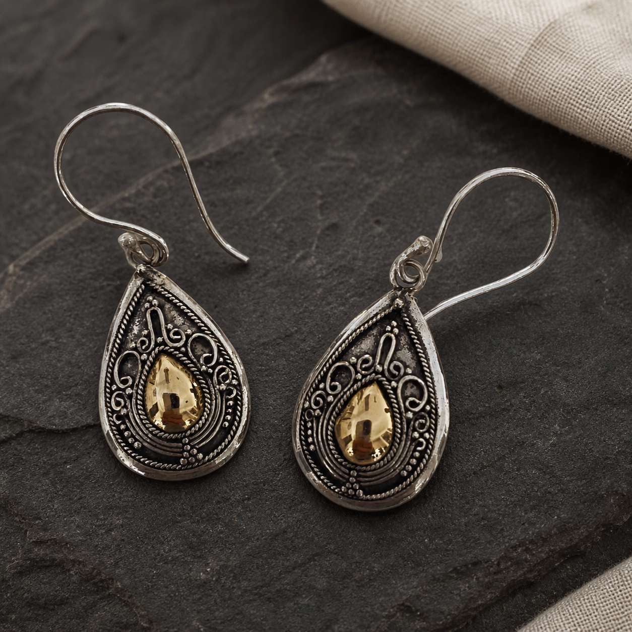 Balinese-style sterling silver and 18ct gold accent earrings displayed on dark natural stone