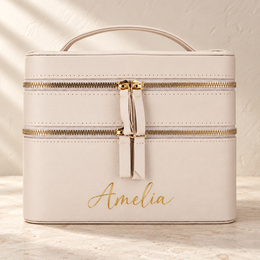 Beige personalised travel makeup case mockup with Amelia in gold script, two zip tiers and a carry handle on a warm neutral background