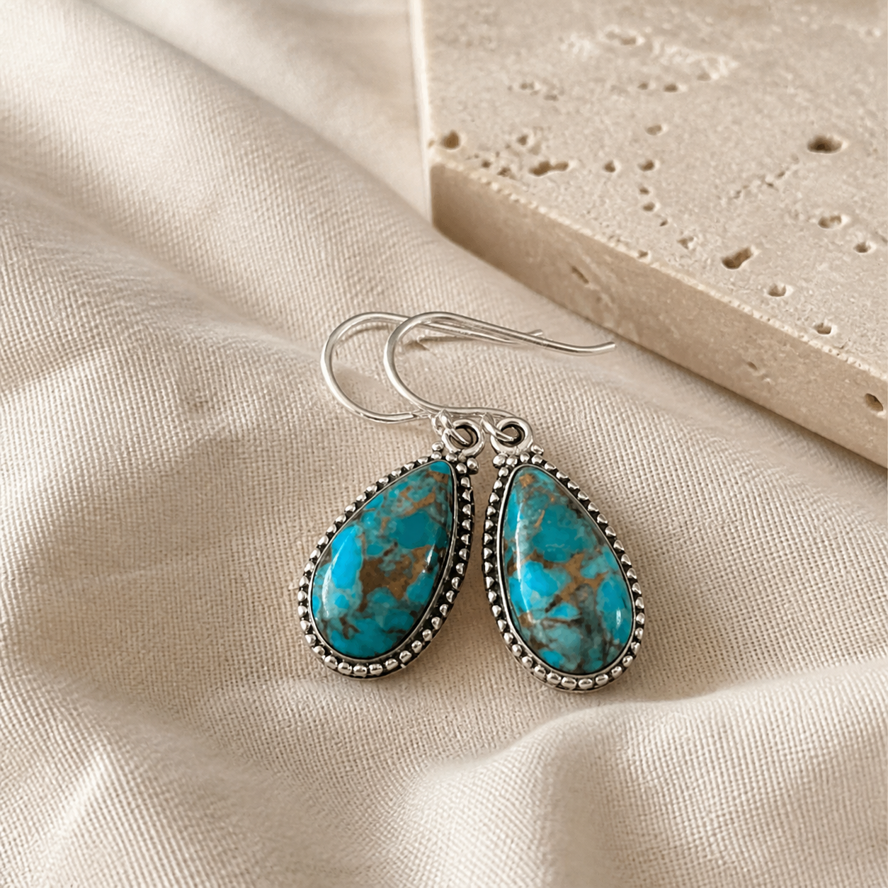 Sterling silver turquoise teardrop earrings displayed on warm ivory linen