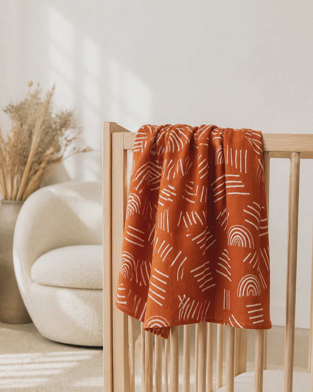 PJ Luxe terracotta baby muslin blanket with white rainbow print in a neutral nursery